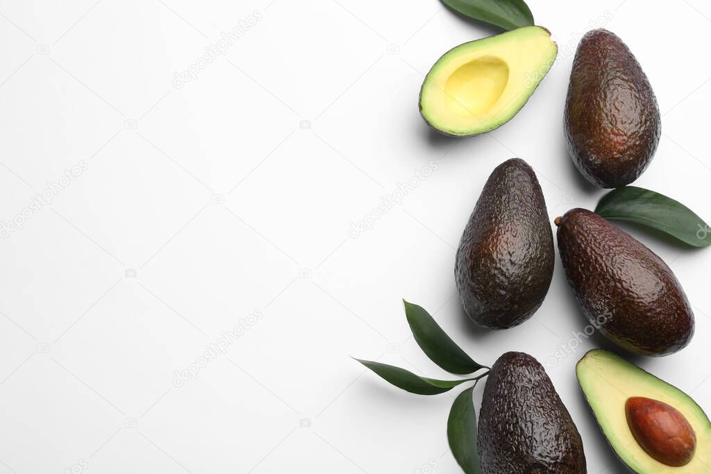 Whole and cut ripe avocadoes with green leaves on white background, top view