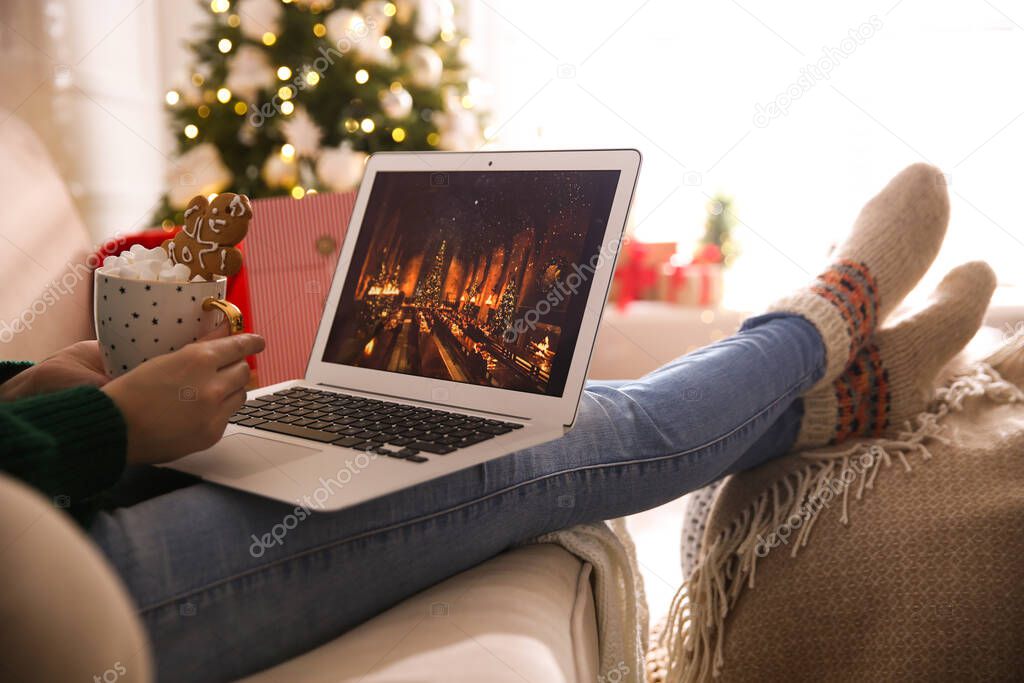 MYKOLAIV, UKRAINE - DECEMBER 25, 2020: Woman with sweet drink watching Harry Potter and Philosopher's stone movie on laptop at home, closeup. Cozy winter holidays atmosphere