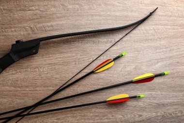 Plastik oklar ve tahta masaya yaylar, düz bir şekilde. Okçuluk spor ekipmanları