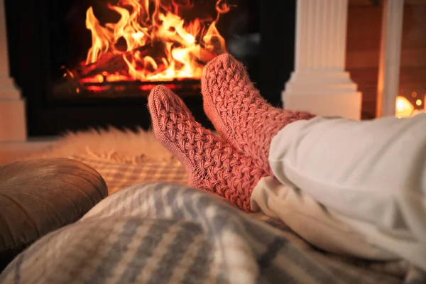 Woman in warm socks having rest near fireplace, closeup