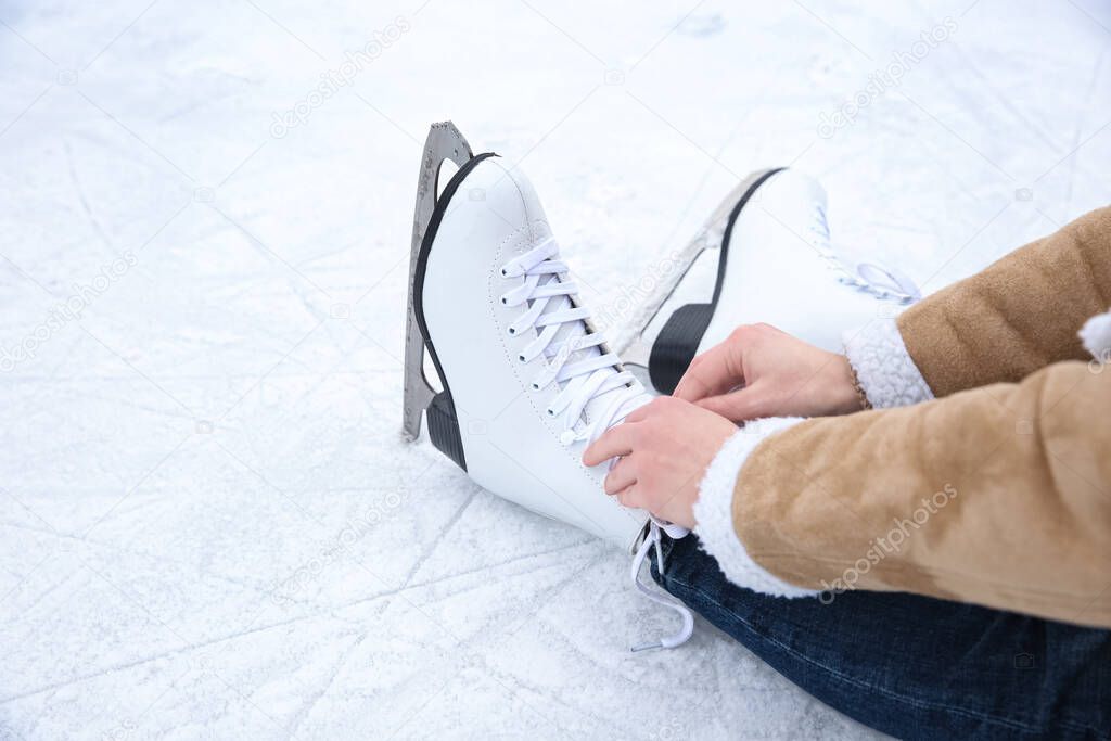 Woman lacing figure skate while sitting on ice rink, closeup