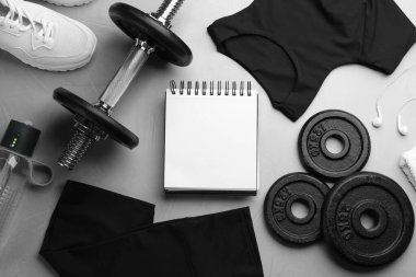 Spor kıyafetleri, defter ve ekipmanlarla gri masanın üzerinde düz kompozisyon vardı. Jimnastik planı