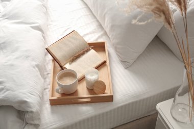 Cup of aromatic coffee, book and candle on bed with soft blanket indoors clipart