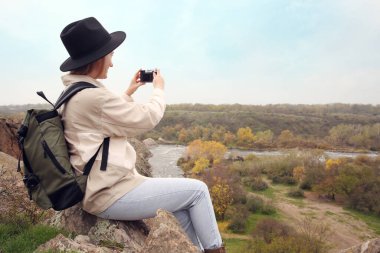 Sırt çantalı gezgin dağ nehri yakınlarında fotoğraf çekiyor. Sonbahar tatili