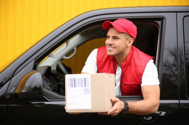 Kurye dışarıdaki arabanın camından paket veriyor.