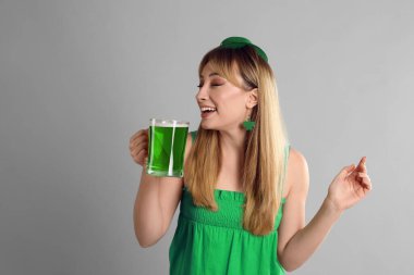 St. Patrick Günü kıyafetli bir kadın açık gri arka planda bira içiyor.