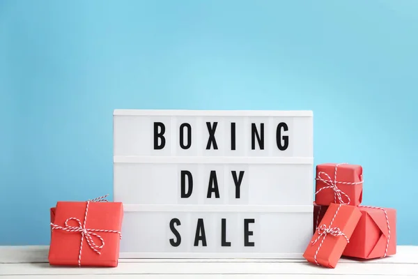 Composition with Boxing Day Sale sign and Christmas gifts on white table against light blue background