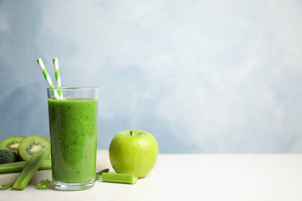 Delicious green juice and fresh ingredients on white table against light blue background, space for text
