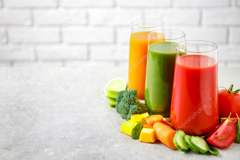 Different tasty juices and fresh ingredients on grey table against brick wall. Space for text