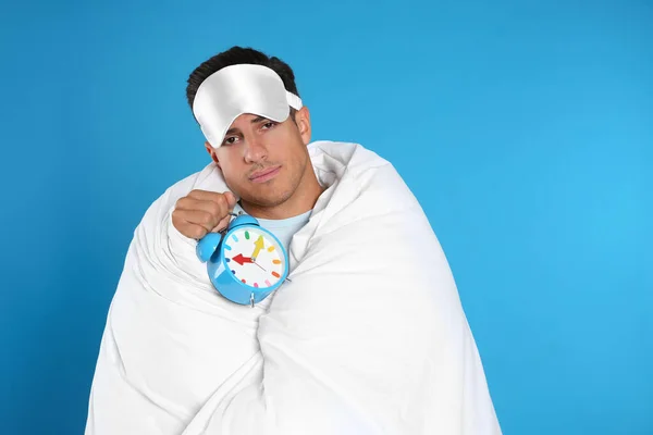 Man Sleeping Mask Wrapped Blanket Holding Alarm Clock Blue Background — Stock Photo, Image