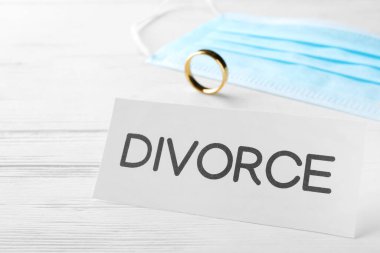 Sözlü boşanma kartı, koruyucu maske ve alyans beyaz ahşap masada, yakın plan.