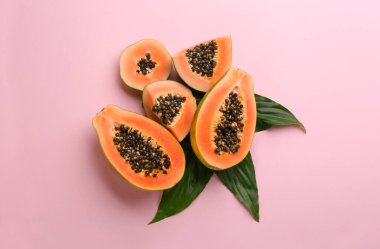 Pembe arka planda yeşil yapraklı taze olgun papaya meyveleri.