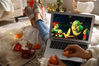 MYKOLAIV, UKRAINE - 25 Aralık 2020: Mandalinalı kadın dizüstü bilgisayarda Shrek the Halls filmini izliyor, yakın plan. Sıcak kış tatili atmosferi