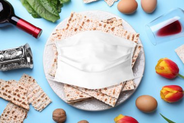 Koronavirüs salgını. Açık mavi zemin üzerinde sembolik Pesach (Hamursuz Bayramı) öğeleri ve koruyucu yüz maskesi ile düz kompozisyon yatıyordu