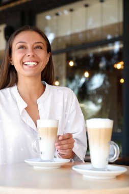 Kafedeki masada kahve içen güzel genç bir kadın.