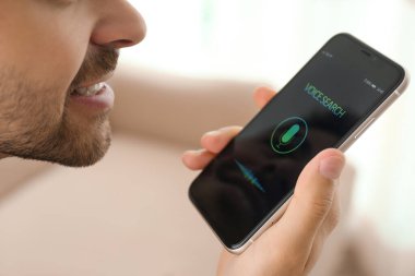 Genç adam akıllı telefondan kapalı alanda ses araması yapıyor.