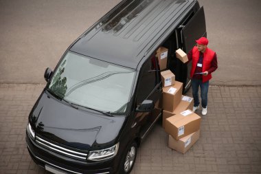 Dağıtım aracının yanında pano ve paket taşıyan bir kurye var.