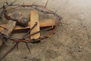 Crown of thorns, wooden cross and hammer with nails on ground, space for text. Easter attributes clipart