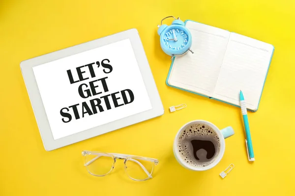 Let\'s Get Started. Flat lay composition with tablet and stationery on yellow background