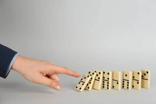 Woman causing chain reaction by pushing domino tile on grey background, closeup. Space for text