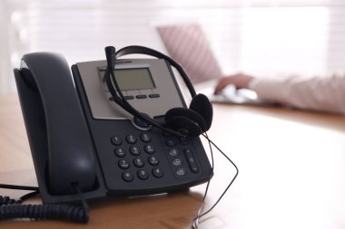 Ofisteki ahşap masada kulaklık takılı bir masaüstü telefonu. Yardım hattı servisi
