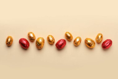 Bej arka planda kırmızı ve altın folyoya sarılı çikolatalı yumurtalar.