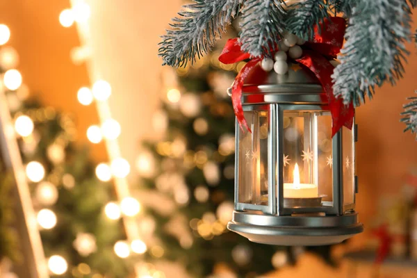 Vintage Christmas lantern with burning candle hanging on fir branch against blurred background. Space for text