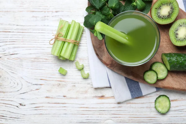 Glass of celery juice and fresh ingredients on white wooden table, flat lay. Space for text