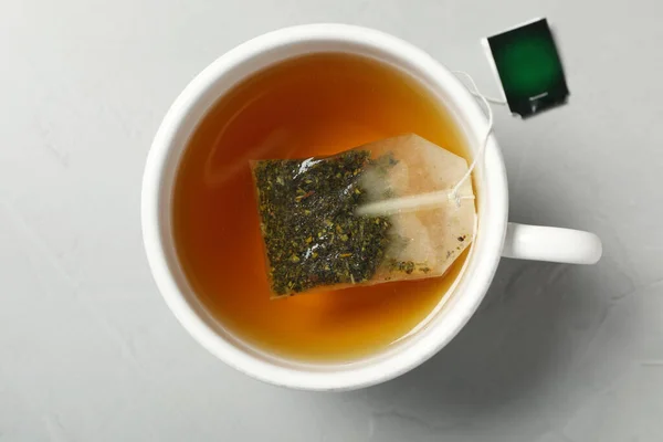 Tea bag in cup of hot water on light grey table, top view