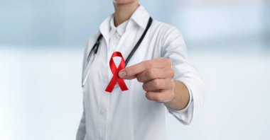 Doktor arka planda kırmızı farkındalık şeridi tutuyor. Yakın plan. Dünya AIDS Hastalıkları Günü