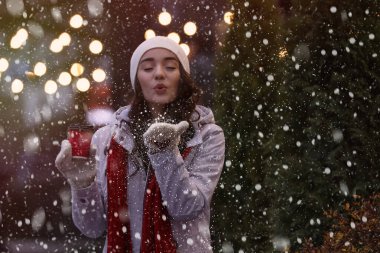Şehir caddesinde akşamları elinde bir bardak içkiyle mutlu genç bir kadın. Noel kutlaması