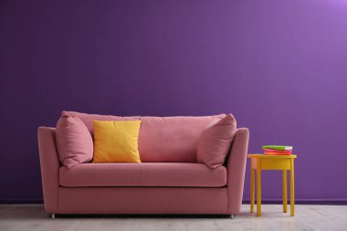 Oturma odasının iç tarafında mor duvarın yanındaki rahat pembe kanepe