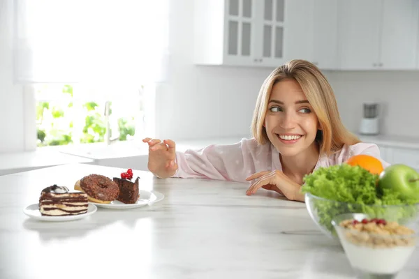 Женщина Выбирает Между Сладостями Здоровой Пищей Белым Столом Кухне — стоковое фото