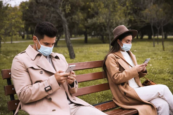 공원에서 스마트폰을 사용하는 남자와 코로나 바이러스 유행병이 유행하는 사회적 거리를 — 스톡 사진