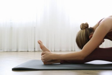 Yoga stüdyosunda dizlerinin üstüne çöküp pratik yapan genç bir kadın. Janu Sirsasana pozu