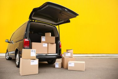 Siyah teslimat minibüsü ve sarı duvarın yanında bir sürü farklı paket var. Mesaj için yer var. Kurye servisi