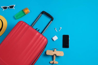 Bavullu düz kompozisyon ve açık mavi arka planda seyahat aksesuarları. Yaz tatili