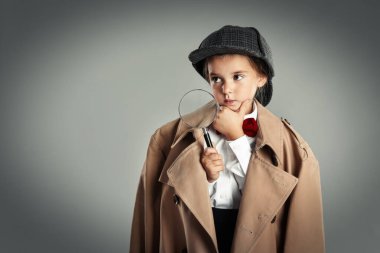 Şapkalı şirin bir çocuk, büyüteçle gri arka planda dedektifçilik oynuyor, mesaj için yer var.