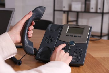 Ofisteki ahşap masada masaüstü telefonu kullanan bir kadın, yakın plan. Yardım hattı servisi