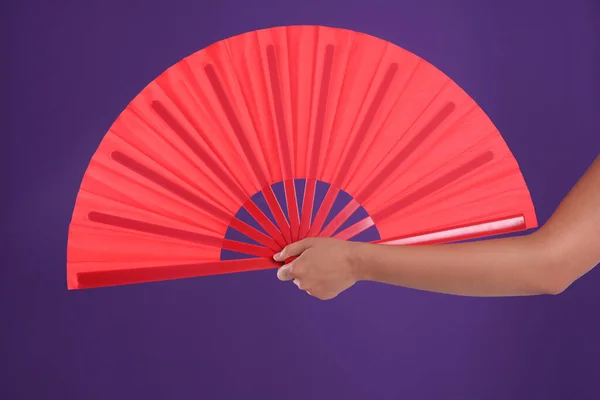 Woman holding red hand fan on purple background, closeup