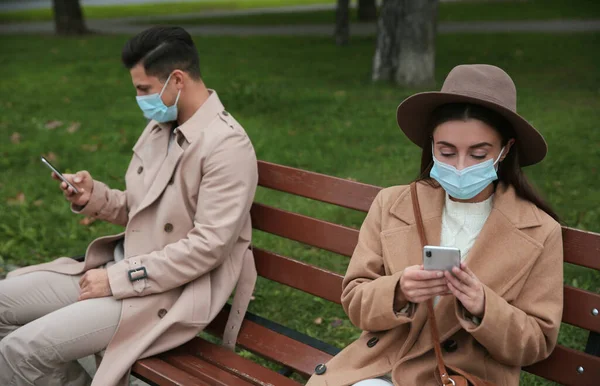 공원에서 스마트폰을 사용하는 남자와 코로나 바이러스 유행병이 유행하는 사회적 거리를 — 스톡 사진
