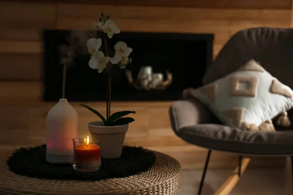 Aroma oil diffuser, burning candle and beautiful potted orchid flower on table in living room. Space for text