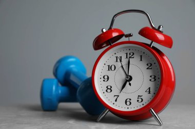Alarm saati ve dambıllar gri arka planda masanın üzerinde. Sabah egzersizi