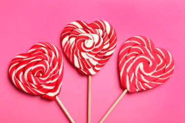 Tatlı kalp şeklinde lolipoplar pembe arka planda, düz yerde. Sevgililer Günü kutlaması