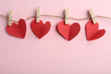 Kırmızı kalpler, ip ve mandallar pembe arka planda, üst görüş alanı metin için. Sevgililer Günü