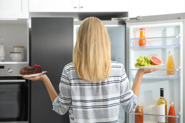 Концепция Выбора Женщина Держит Тарелки Фруктами Сладостями Рядом Холодильником Кухне — стоковое фото