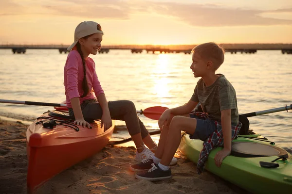 日落时 快乐的孩子们坐在河边的皮划艇上 夏令营 — 图库照片
