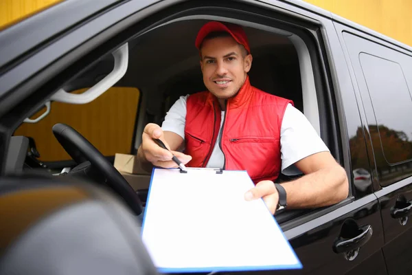 Courier giving clipboard with documents out of car window outdoors