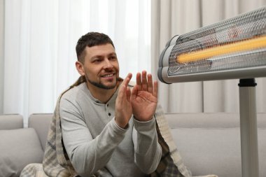 Evde elleri ısıtan adam elektrikli kızılötesi ısıtıcının yanında.
