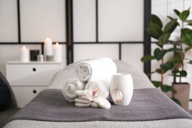 Havlular, aroma lambası, orkide çiçeği ve taşlar kaplıca salonundaki kanepede.